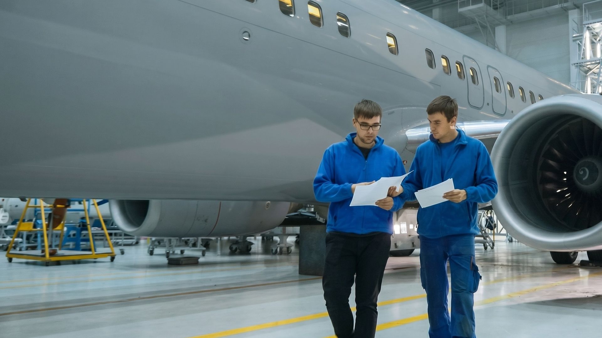 Two aircraft maintenance engineers reviewing documents beside a jet airliner in a hangar